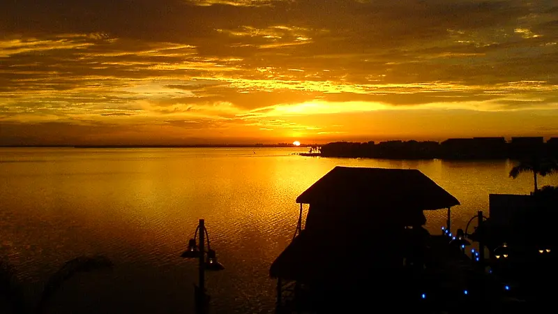 Sol dorado sobre la laguna Nichupté al atardecer, con una palapa en primer plano, en Cancún