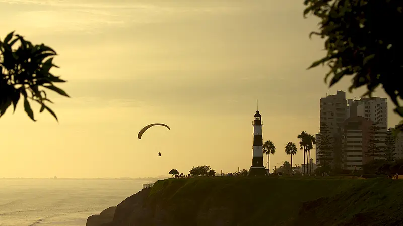 Parapentes volando al atardecer sobre el malecón de Miraflores y su faro, en Lima