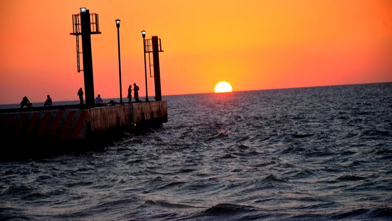 Personas en el muelle de Celestún mirando el sol ponerse sobre el Golfo de México