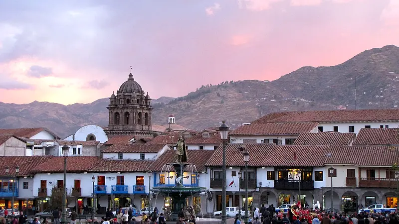 Plaza de Armas de Cusco al atardecer, con gente paseando y el cielo rosado sobre los cerros