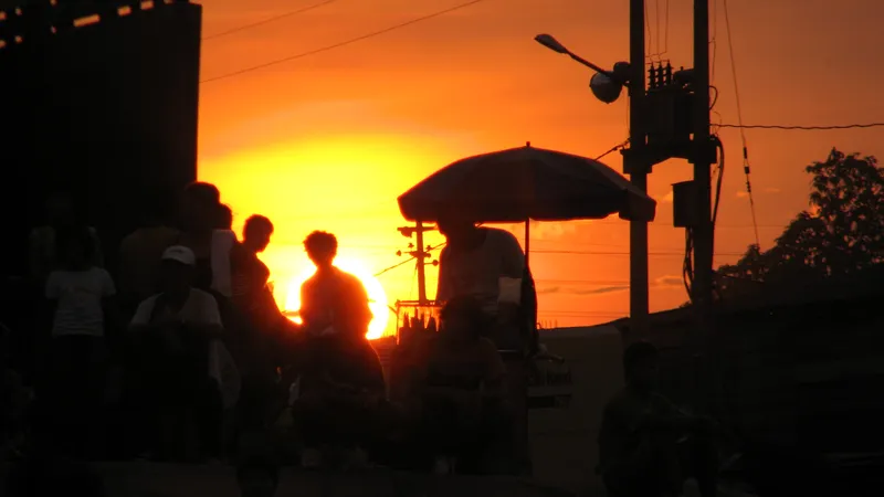 Siluetas de personas y un puesto con sombrilla frente al sol del atardecer en el Puerto Henry de Iquitos