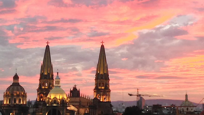 Las torres y la cúpula de la Catedral de Guadalajara iluminadas, contra un cielo rosa y naranja del atardecer