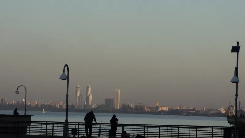 Personas apoyadas en la baranda de la costanera de Rosario, junto al río Paraná, al caer la tarde
