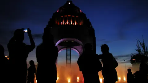 Siluetas de personas fotografiando el Monumento a la Revolución iluminado al caer la tarde, en Ciudad de México