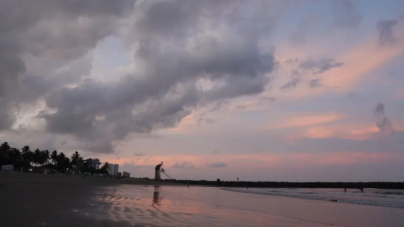 Una persona caminando por la arena mojada de Playa Mocambo bajo un cielo nublado y rosado al caer la tarde, en Veracruz