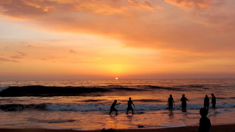 Personas en la orilla de Playas de Tijuana mirando el sol ponerse sobre el Pacífico