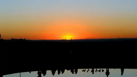Siluetas de personas sentadas en el Templo de Debod mirando el sol ponerse sobre la Casa de Campo, en Madrid