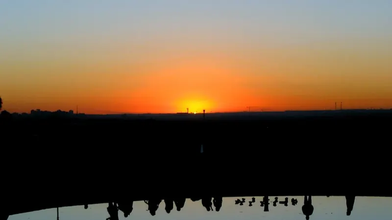 Siluetas de personas sentadas en el Templo de Debod mirando el sol ponerse sobre la Casa de Campo, en Madrid