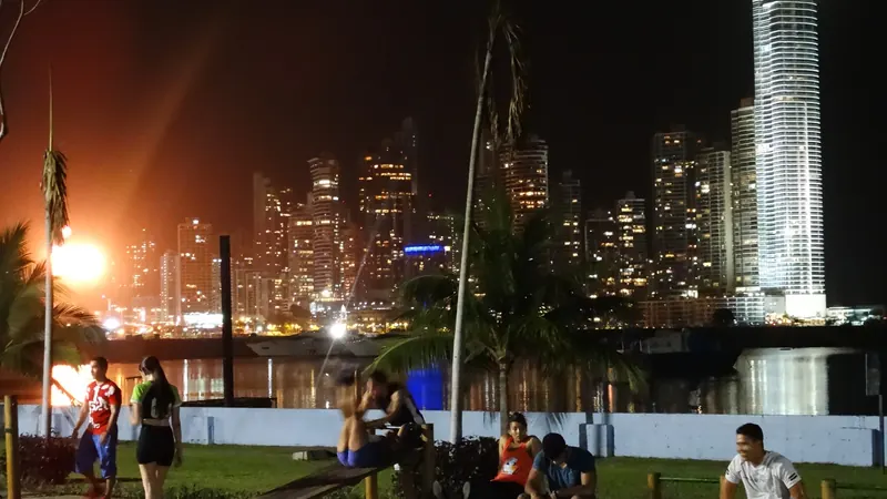 Gente paseando y sentada en la Cinta Costera de Ciudad de Panamá al anochecer, con los rascacielos iluminados al fondo