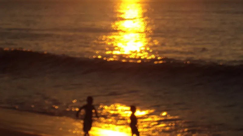 Siluetas de dos niños corriendo por la orilla de una playa de Viña del Mar, con el reflejo del sol poniente en el agua