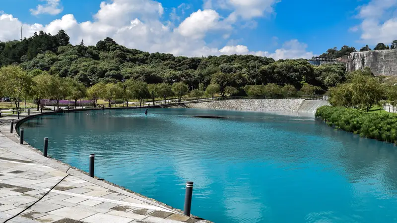 Lago de agua azul del Parque La Mexicana, en Santa Fe, rodeado de árboles y un andador de piedra