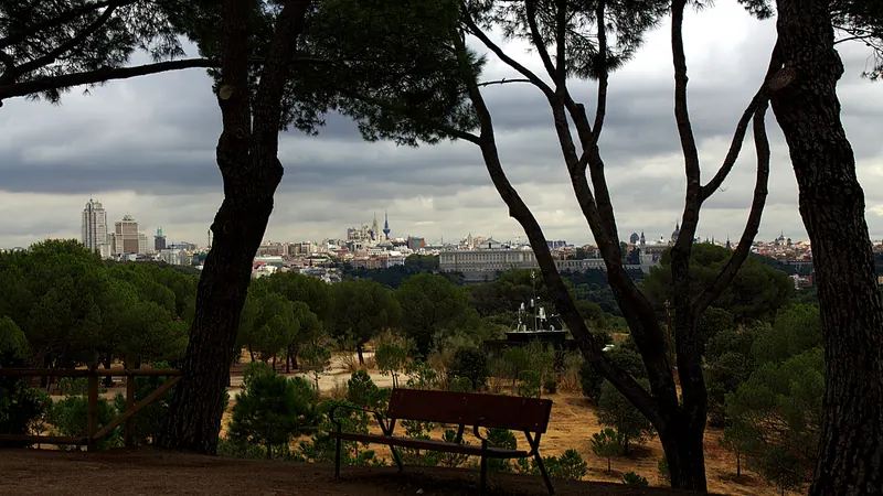 Vista de Madrid entre pinos desde el Cerro Garabitas, en la Casa de Campo, con un banco vacío en primer plano y los edificios del centro al fondo