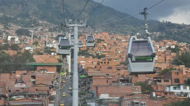 Cabinas del Metrocable de Medellín sobre las casas de ladrillo de una ladera, con las montañas al fondo