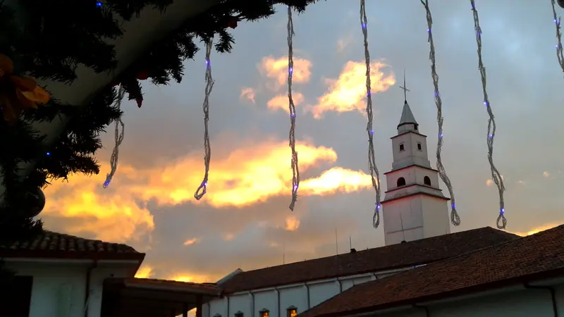 Nubes naranjas del atardecer sobre la torre blanca y los tejados de Monserrate, con luces de Navidad colgando del alero