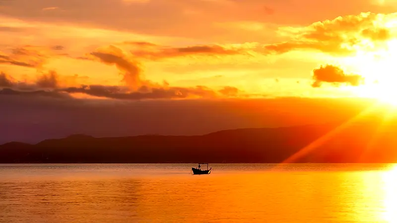 Sol dourado se pondo sobre a baía na Praia da Daniela, em Florianópolis, com um barco ao longe